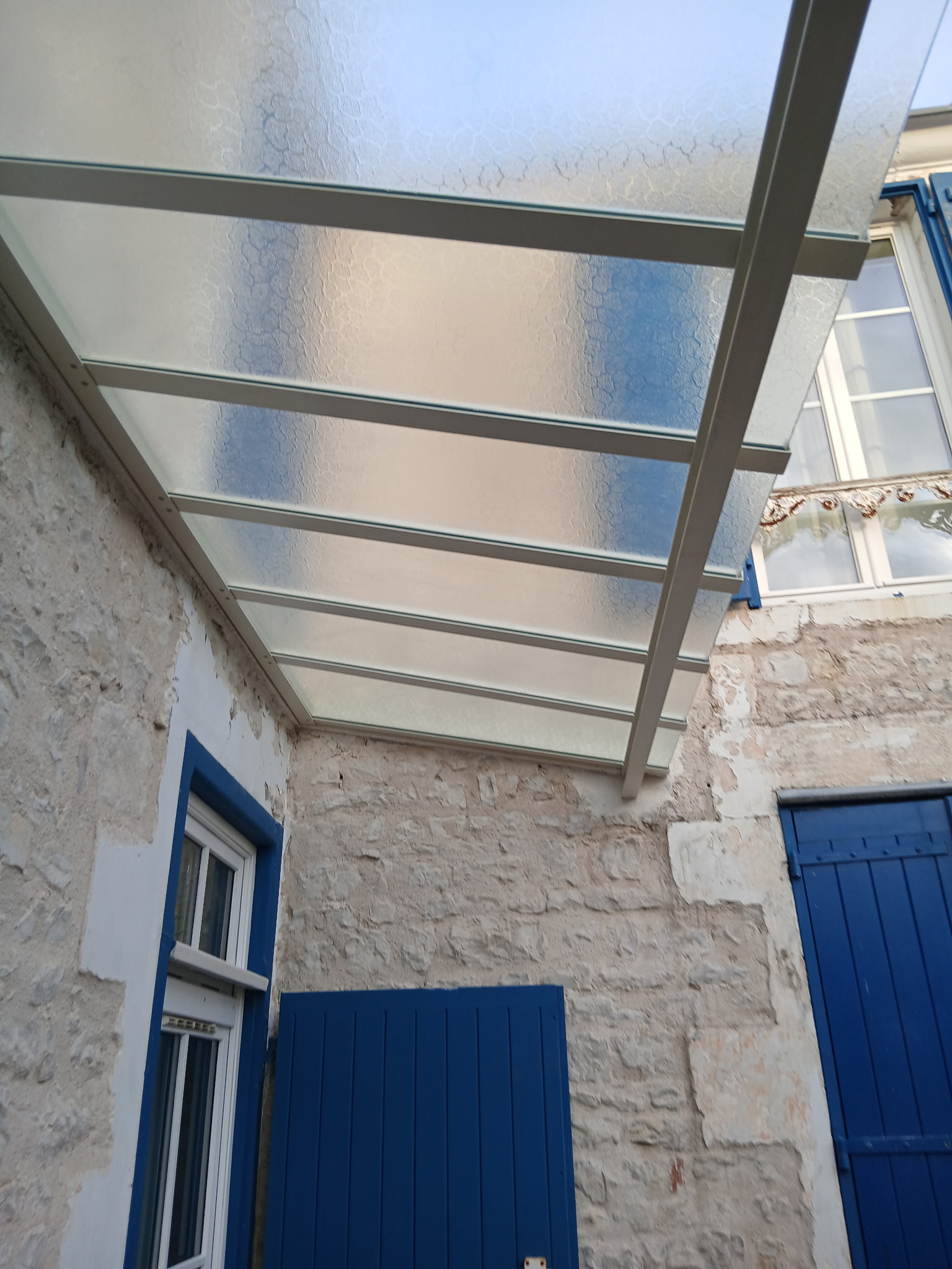 Marquise à l'ancienne en verres cathédrales sur maison en pierre, structure thermolaquée